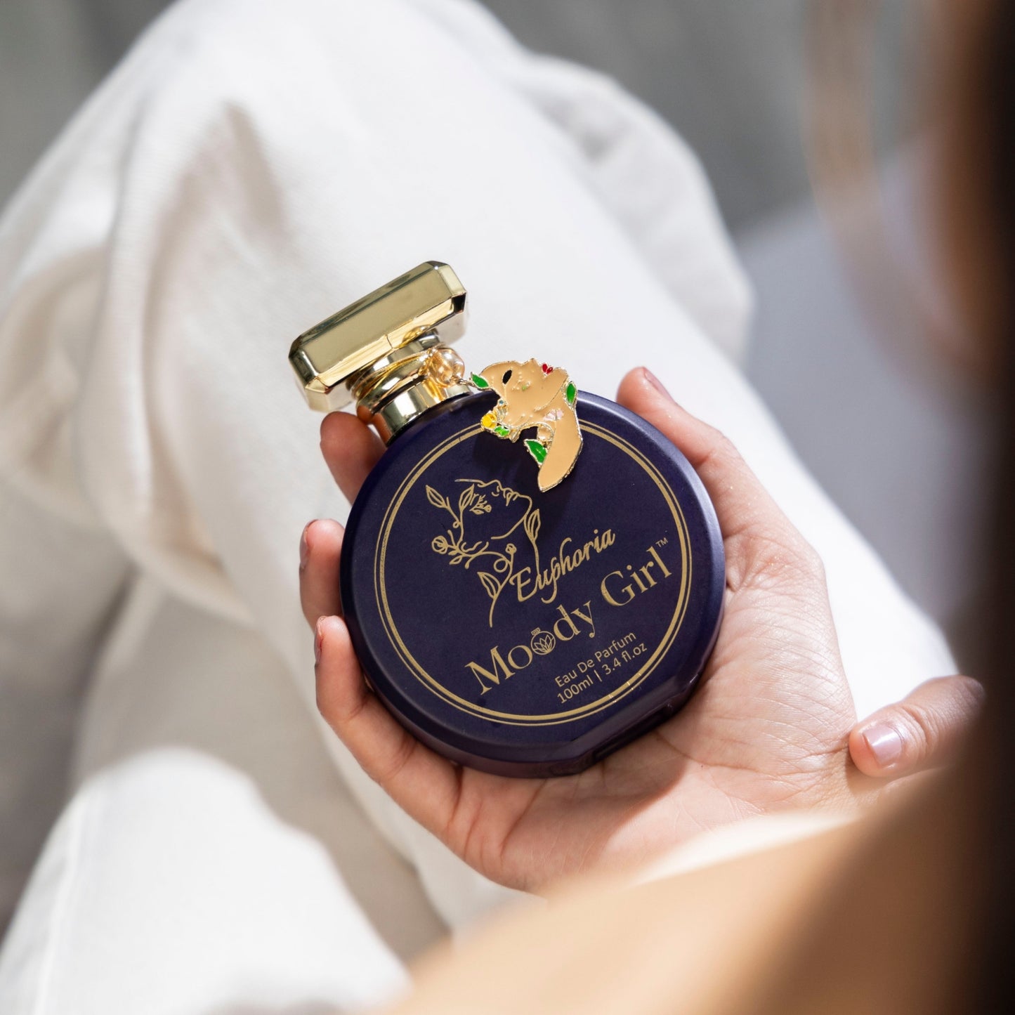 Hand holding a Moody Girl Euphoria 100ml perfume bottle with gold cap