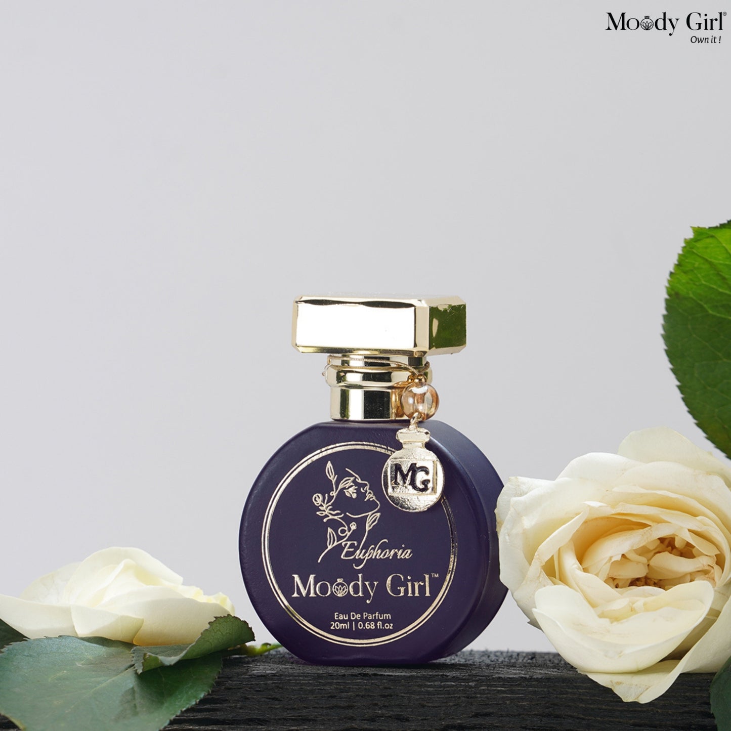 Perfume bottle labeled 'Moody Girl' with white roses on a light gray background