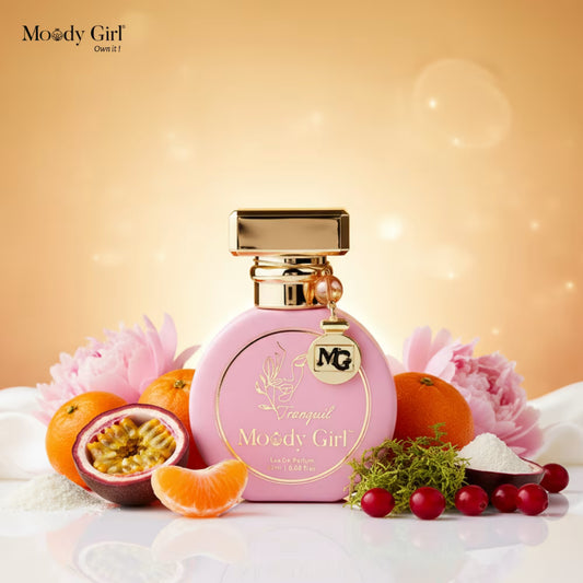 Pink perfume bottle with gold accents on a decorative background with fruits and flowers, featuring the brand 'Moody Girl'.