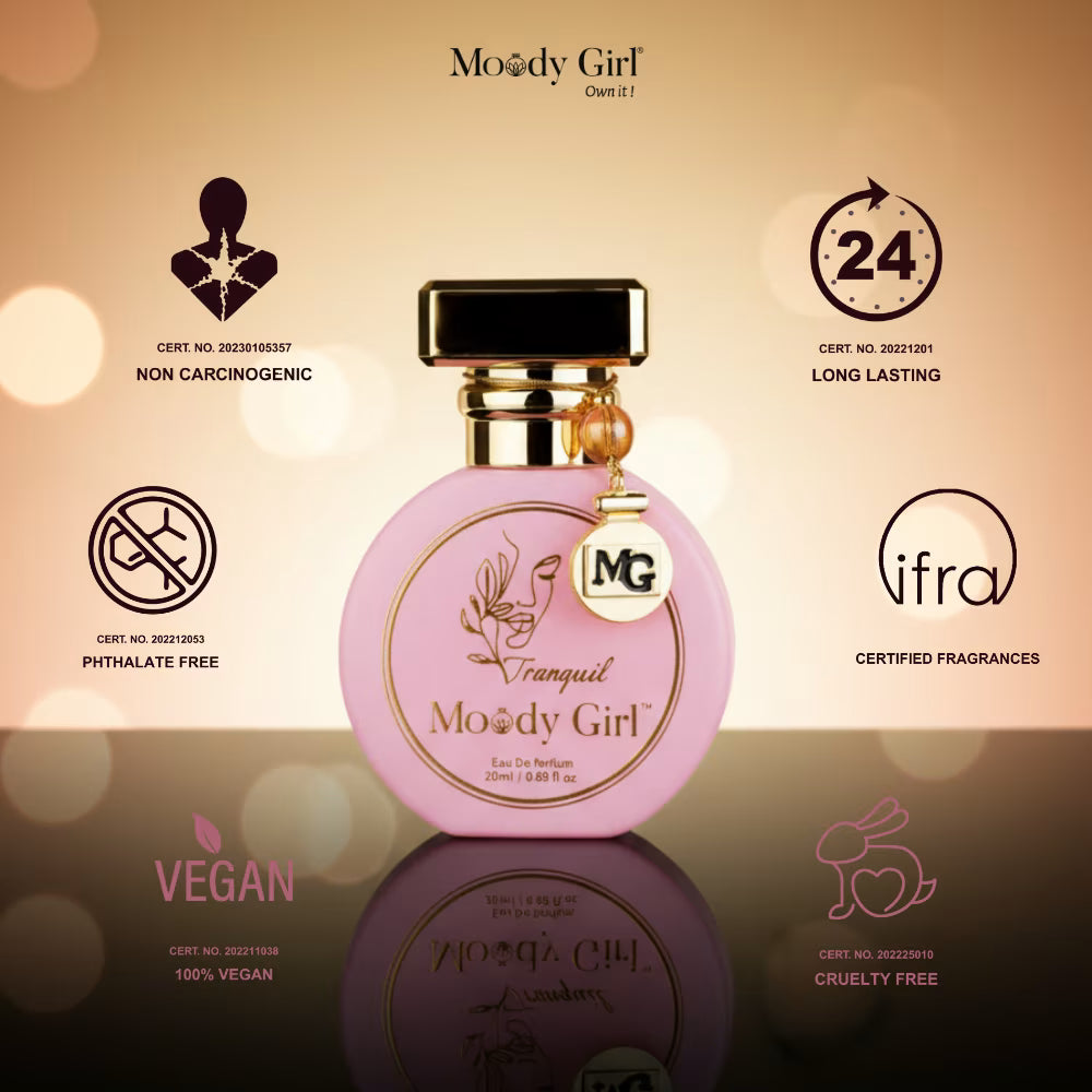Pink perfume bottle with gold cap on a reflective surface, featuring Moody Girl branding and certification icons.