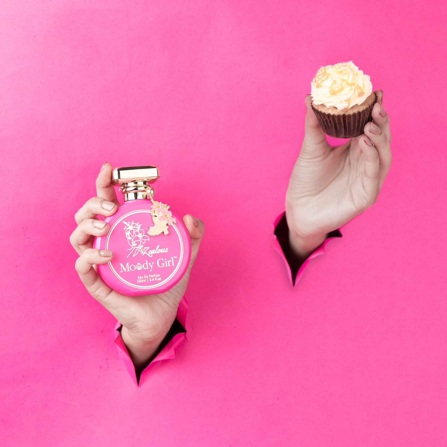 Pink 'Moody Girl' perfume bottle and cupcake held against a pink background