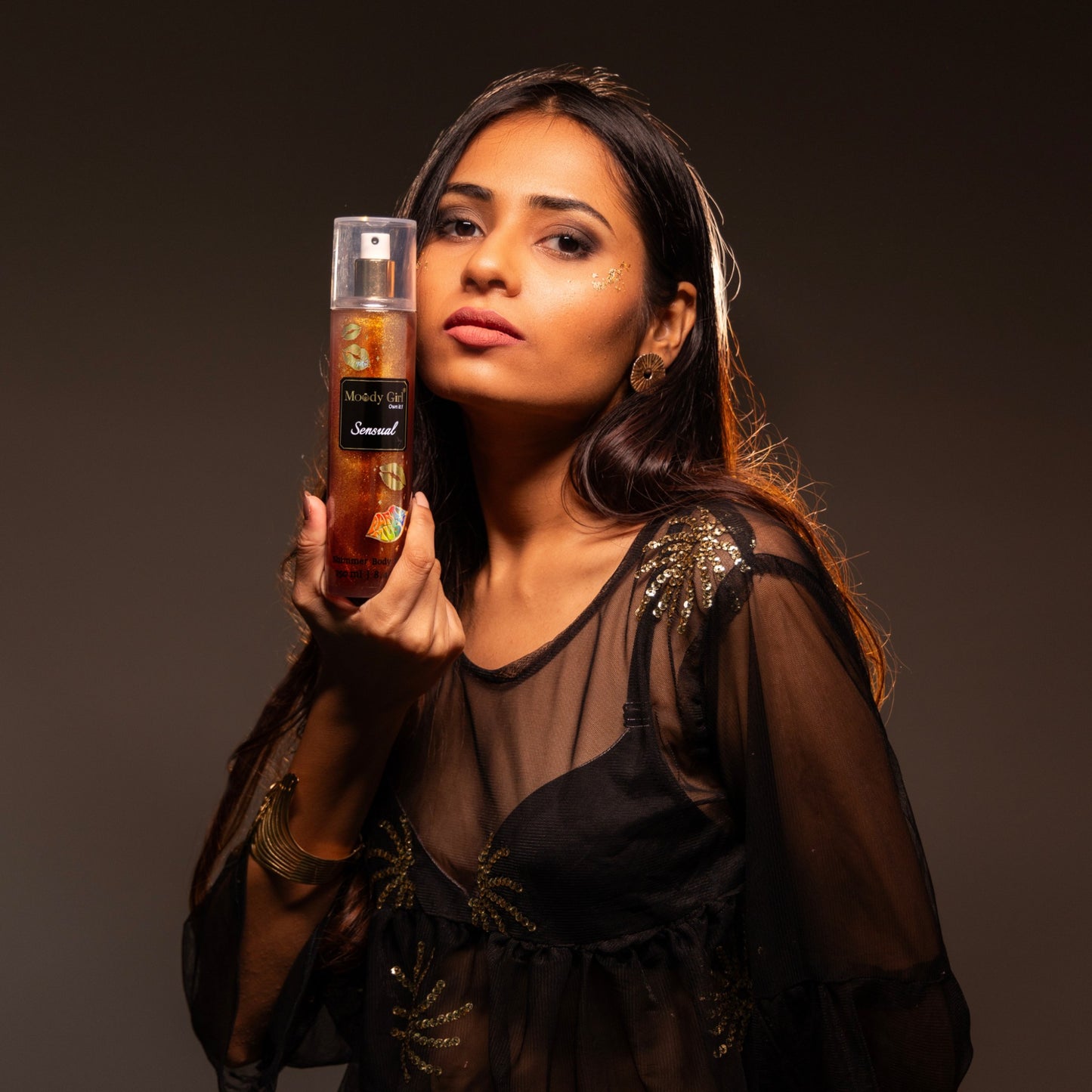 Woman holding a bottle of 'Moody Girl' perfume against a dark background