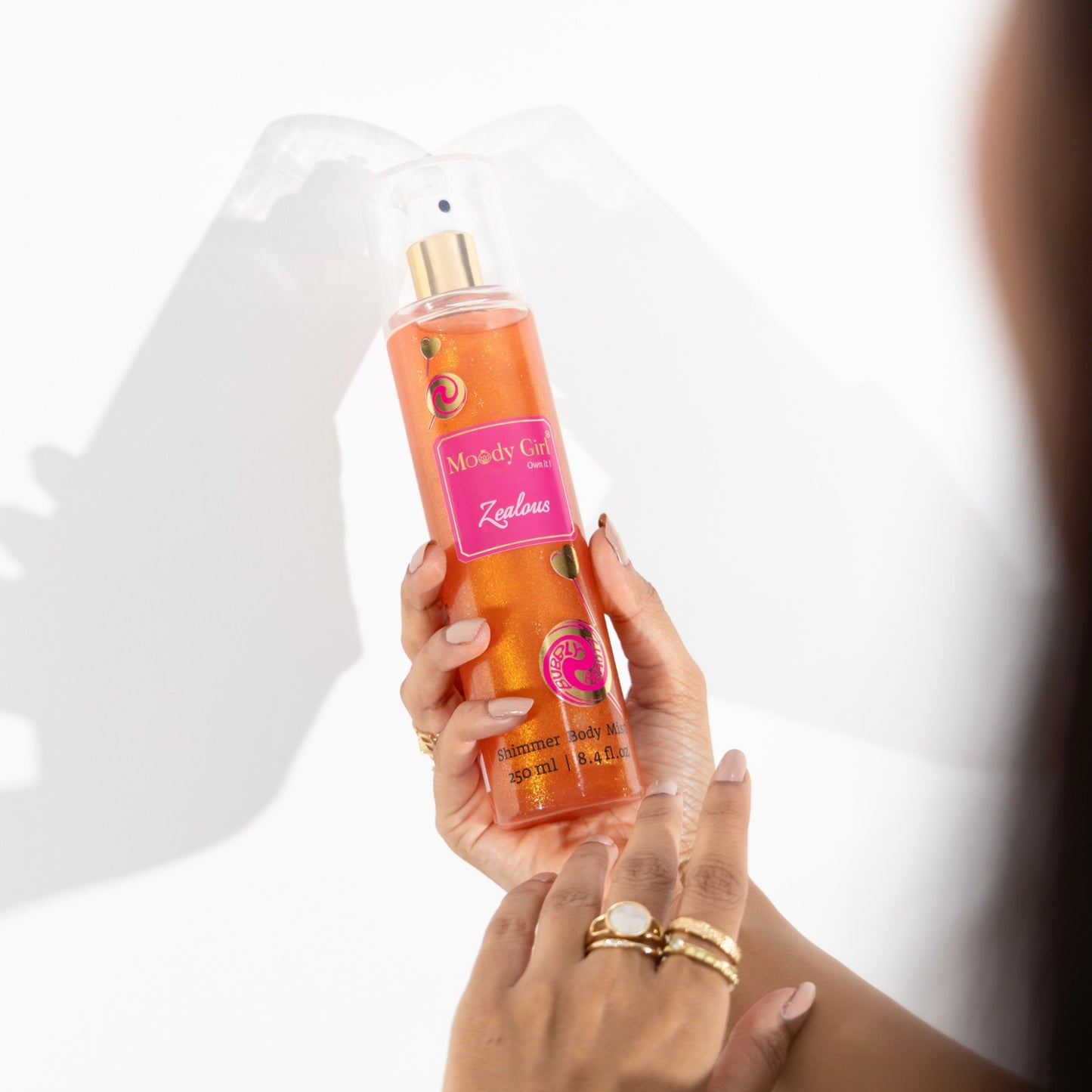 Hand holding a bottle of 'Moody Girl' body spray with a white background