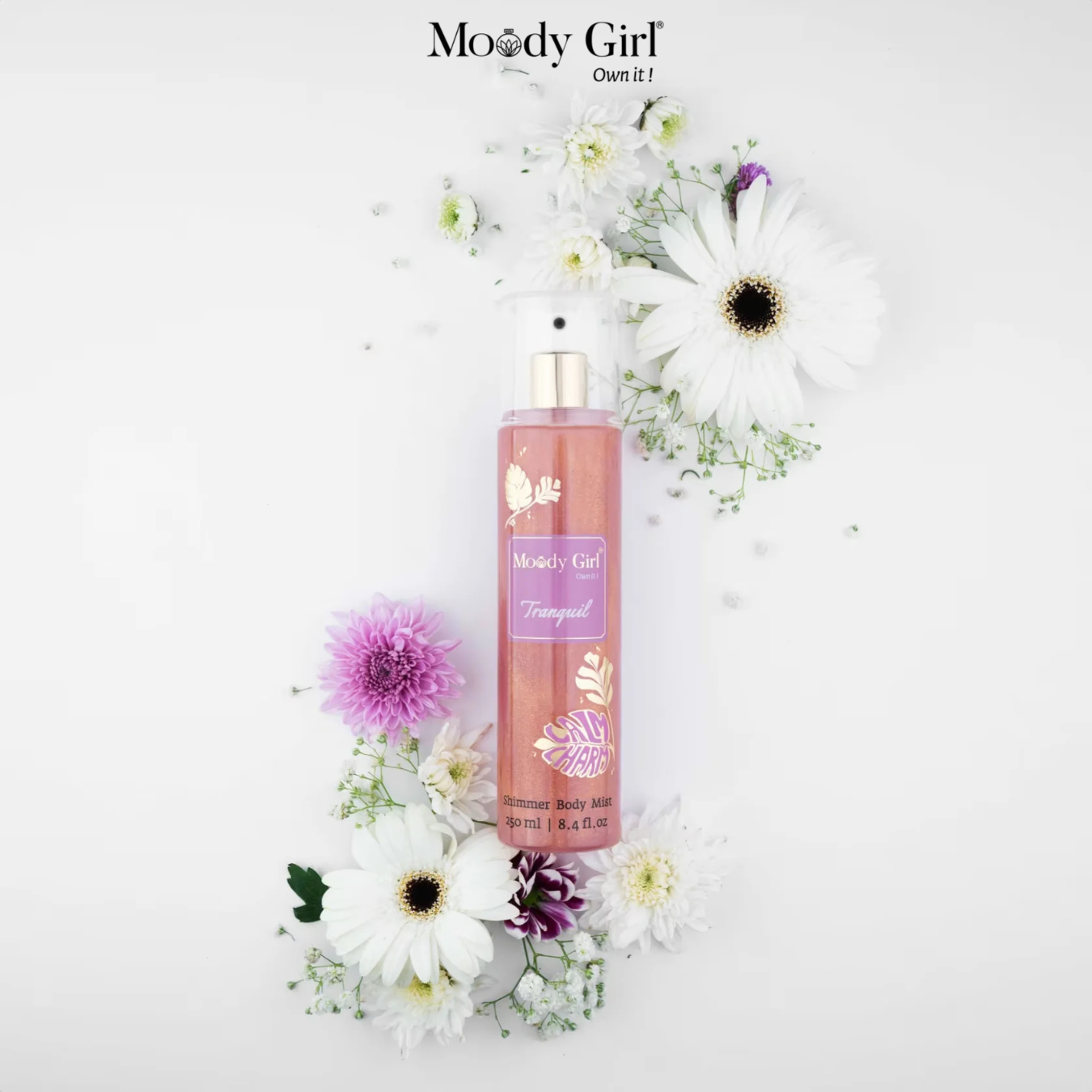 Moody Girl body spray surrounded by flowers on a white background