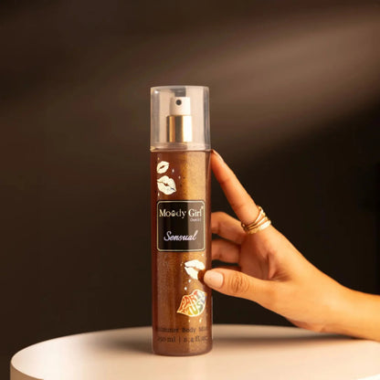Hand holding a 'Moody Girl Sensual' body spray bottle against a dark background