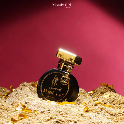 Perfume bottle labeled 'Moody Girl' on a sand-like surface with a red background