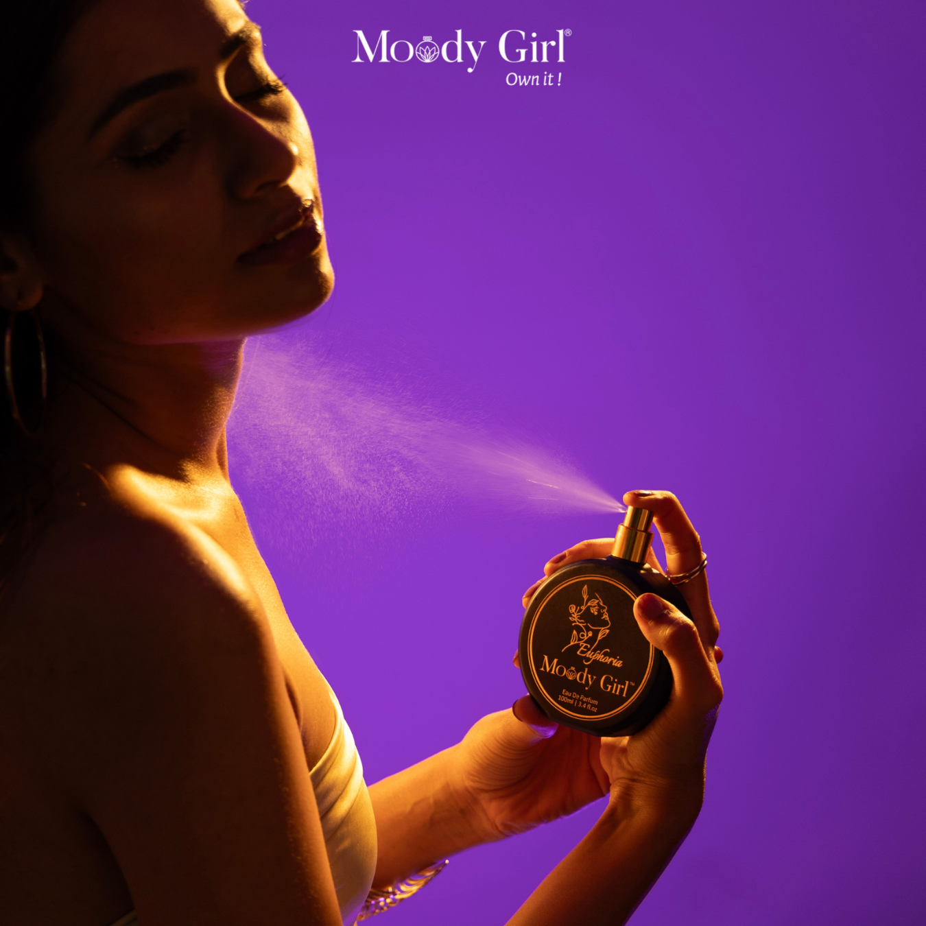Woman spraying perfume from a Moody Girl bottle against a purple background