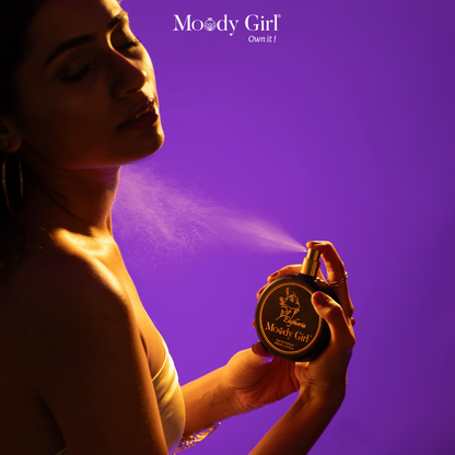 Woman spraying perfume from a Moody Girl bottle against a purple background