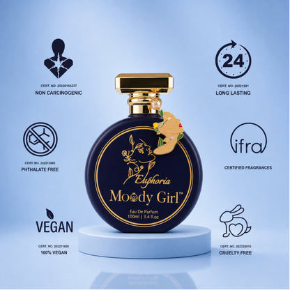 A round dark blue perfume bottle with a gold cap and gold lettering reading 'Euphoria Moody Girl' stands on a white pedestal against a light blue background. Surrounding the bottle are certification-style icons and text for non carcinogenic, long lasting, phthalate free, certified fragrances, vegan, and cruelty free.