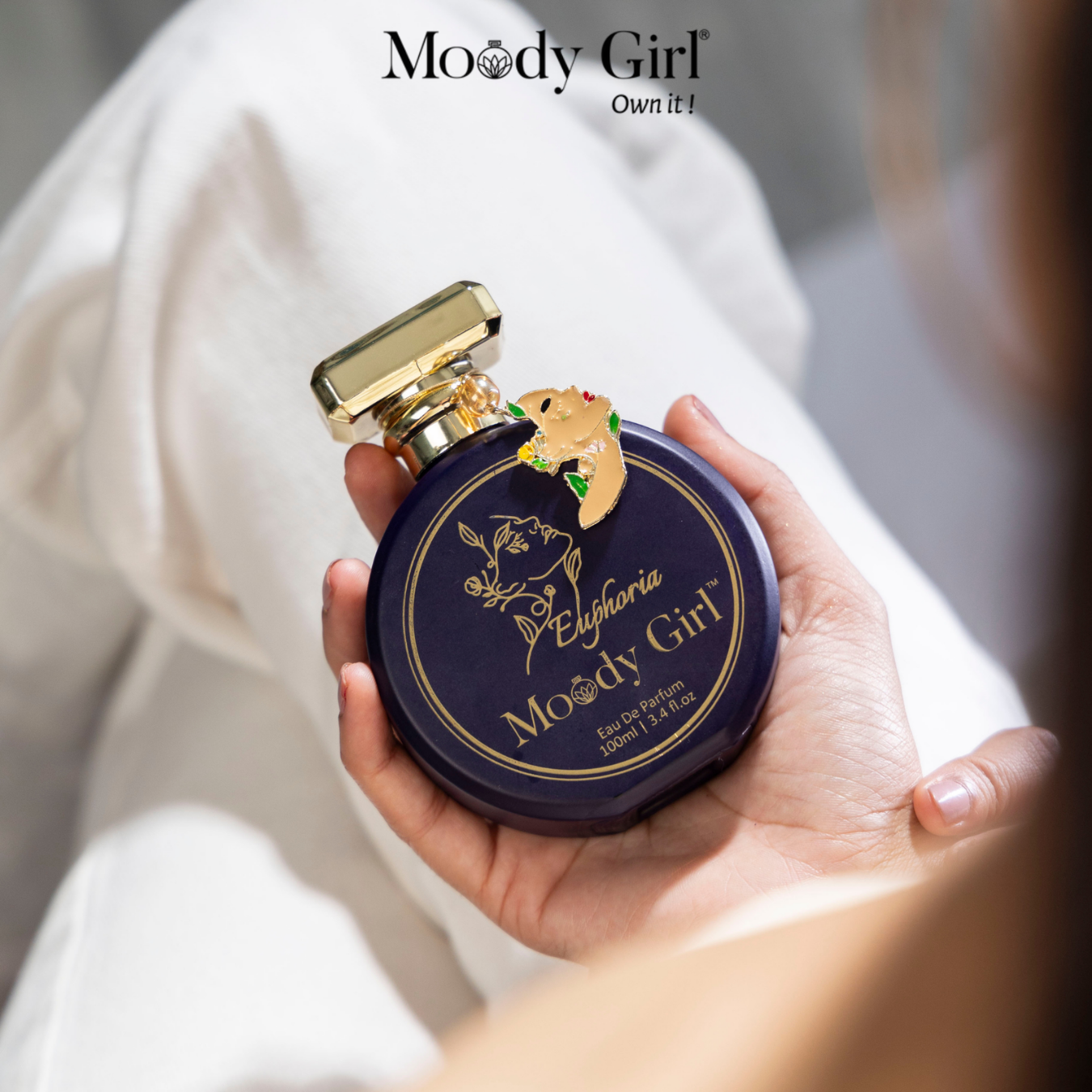 Hand holding a Moody Girl perfume bottle with gold cap