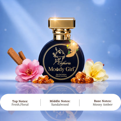 A bottle of Euphoria 'Moody Girl' Eau De Parfum centered on a blue gradient background, flanked by pink and yellow flowers, cinnamon sticks, and amber crystals. A white text banner at the bottom lists the top, middle, and base notes.