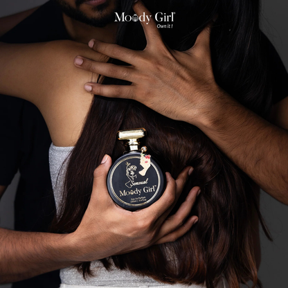 Person holding a Moody Girl perfume bottle with another person embracing them.