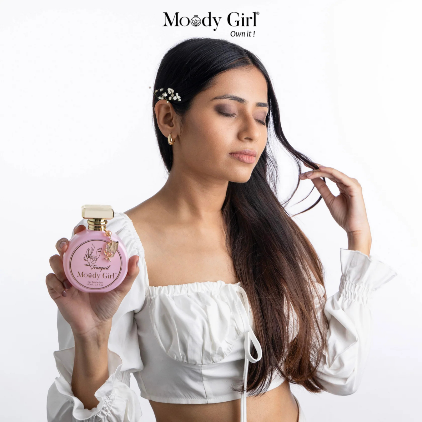 Woman holding a pink 'Moody Girl' perfume bottle with the brand name displayed.