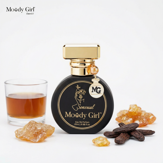 Moody Girl perfume bottle with a glass of liquid and natural elements on a white background