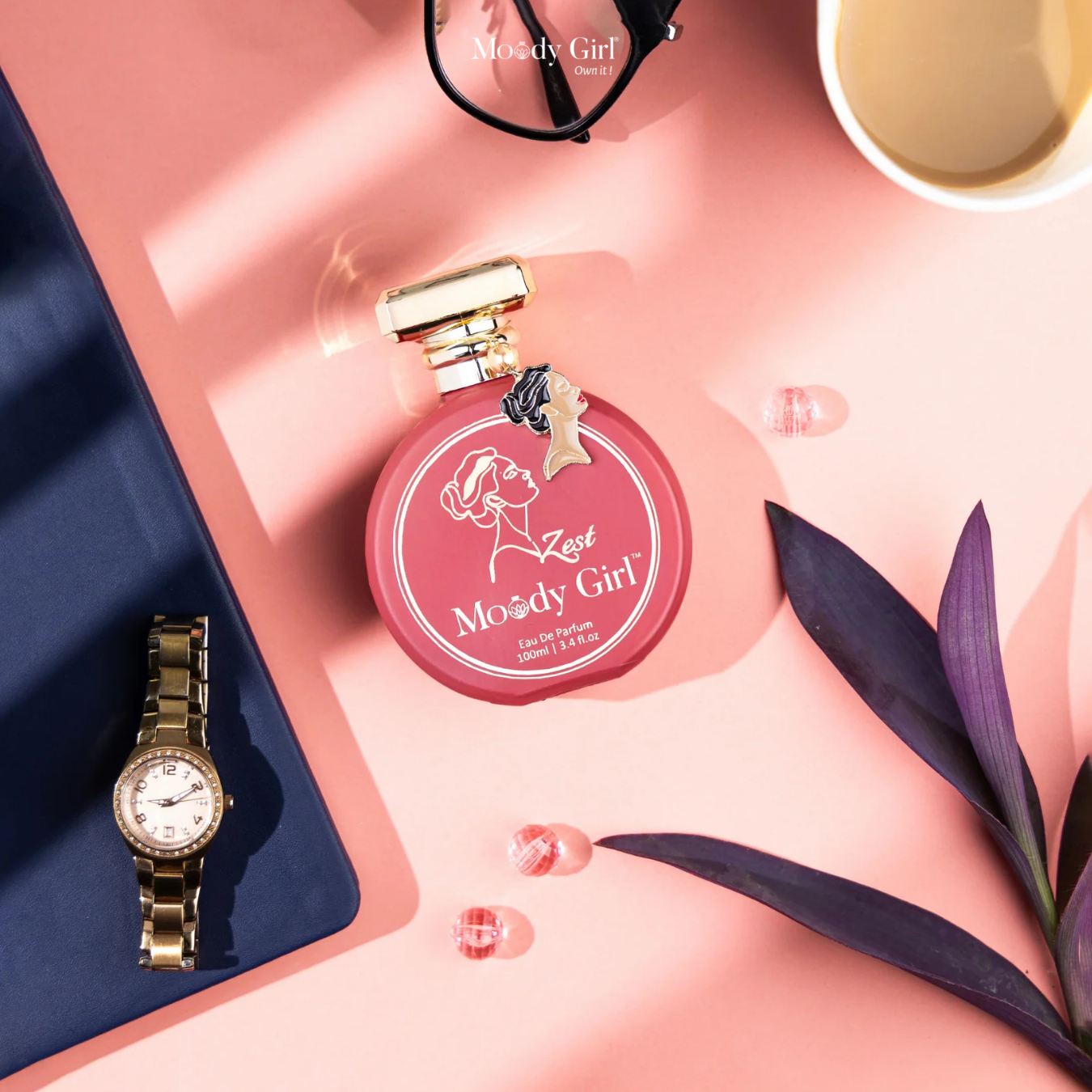Pink perfume bottle with gold cap and watch on a pink surface