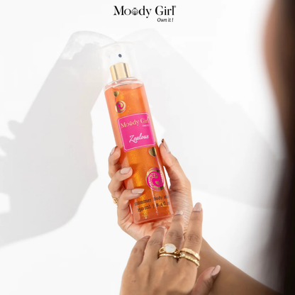 Hand holding a bottle of 'Moody Girl' body spray with a white background