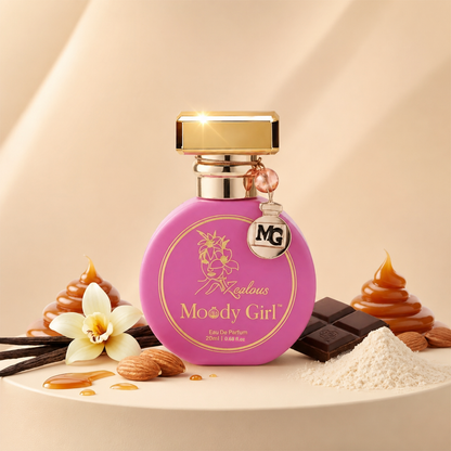 A round pink perfume bottle labeled 'Fascinating Moody Girl' with a gold cap, styled on a beige surface with caramel swirls, chocolate pieces, vanilla flower, almonds, and white powder.