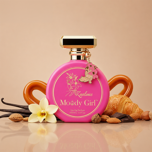 A pink perfume bottle labeled 'Zelons Moody Girl' with gold detailing and a hanging flower charm, styled on a beige surface with vanilla flowers, almonds, and a croissant around it.