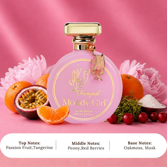 A pink perfume bottle labeled 'Tranquil Moody Girl' with a gold cap, styled with citrus fruits, flowers, and berries on a pink background. Text at the bottom lists the top, middle, and base notes.
