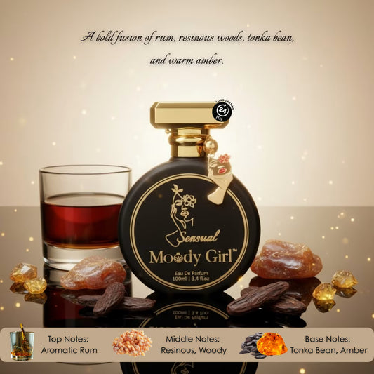 Perfume bottle labeled 'Sensual Moody Girl' with a glass of red liquid and amber stones on a reflective surface.