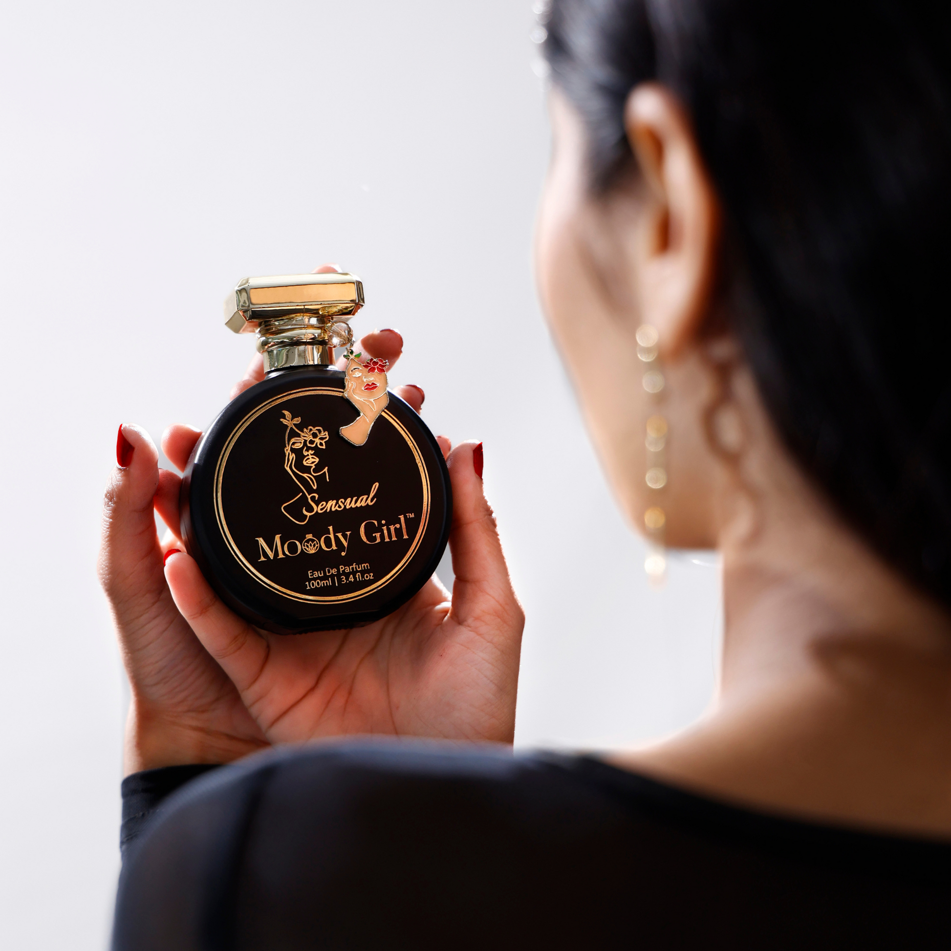 Person holding a 'Sensual Moody Girl' perfume bottle with a plain background