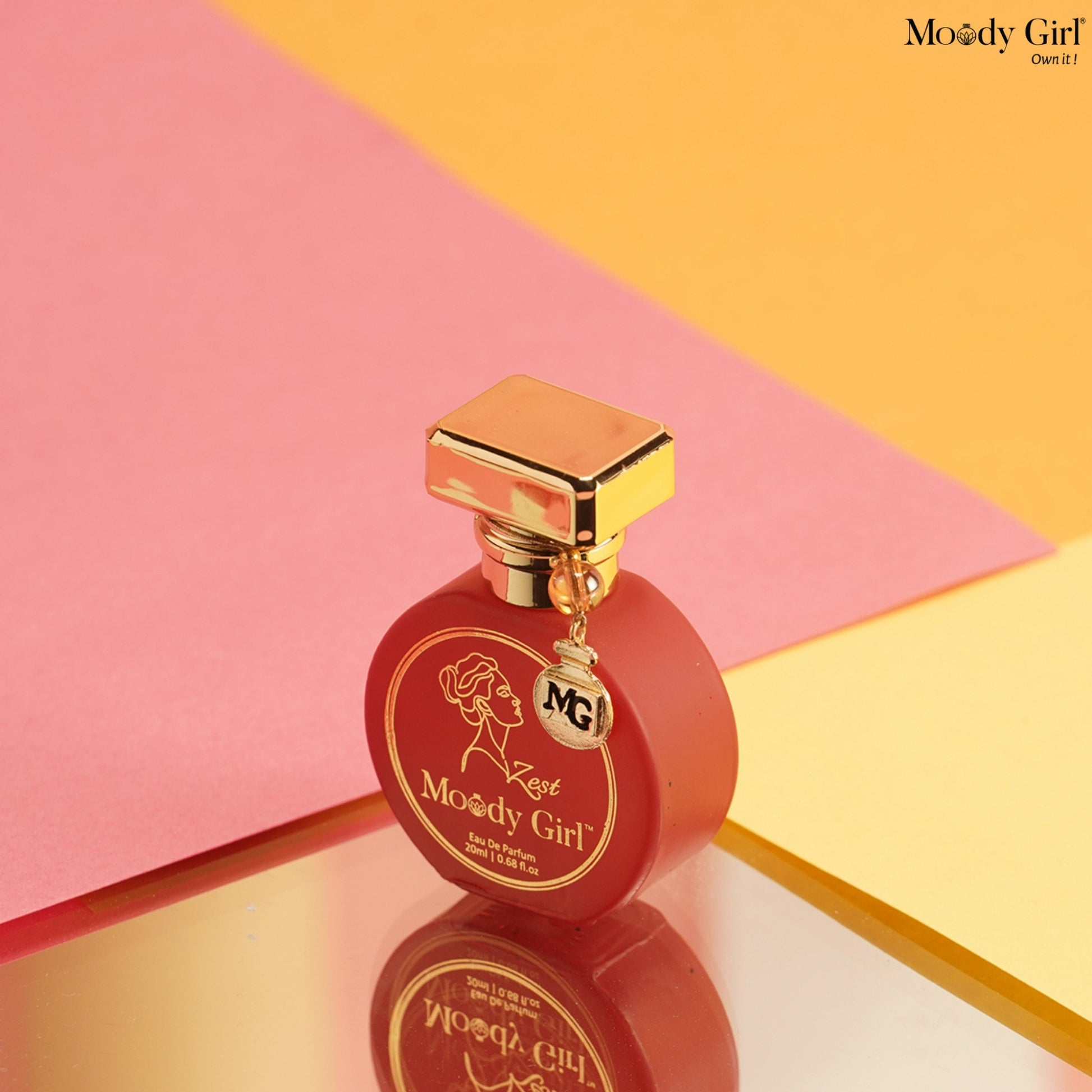 Red perfume bottle with gold cap on a pink and yellow geometric background, featuring 'Moody Girl' branding.