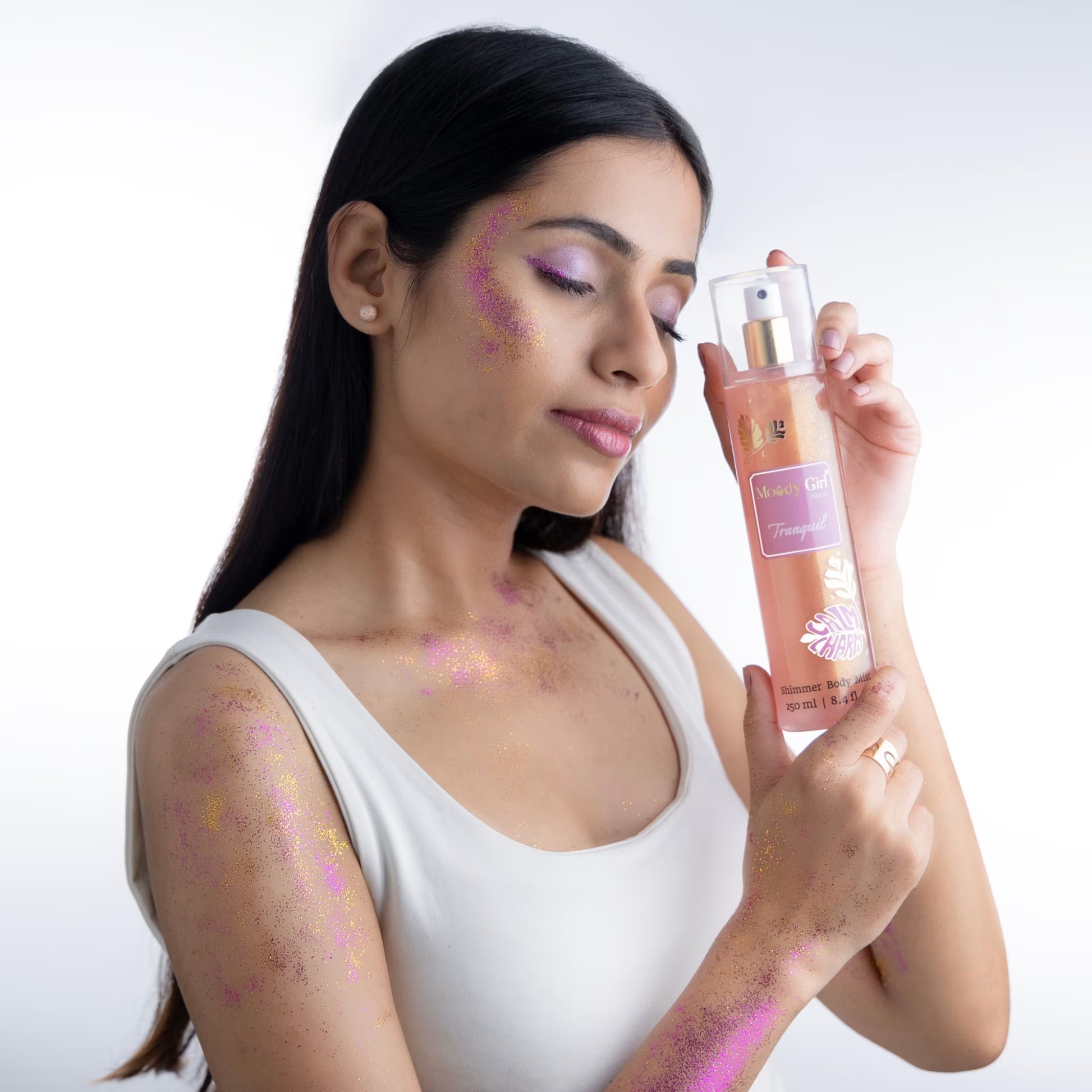 Woman holding Tranquil shimmer body mist with visible glitter on a white background