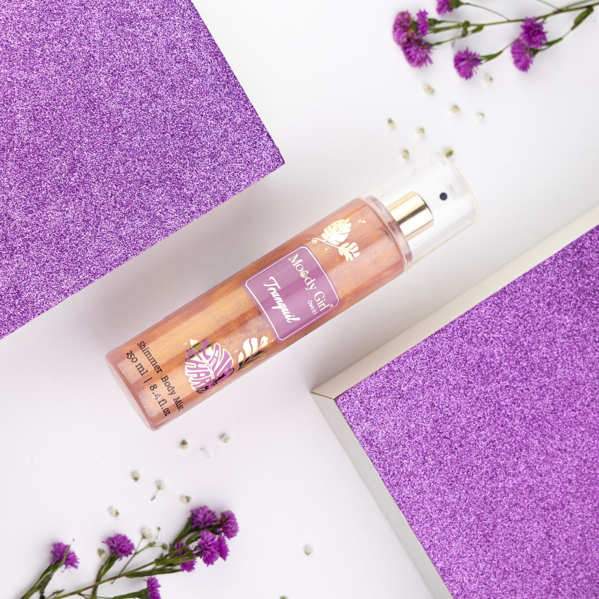 Body spray bottle on a white surface with purple accents and flowers