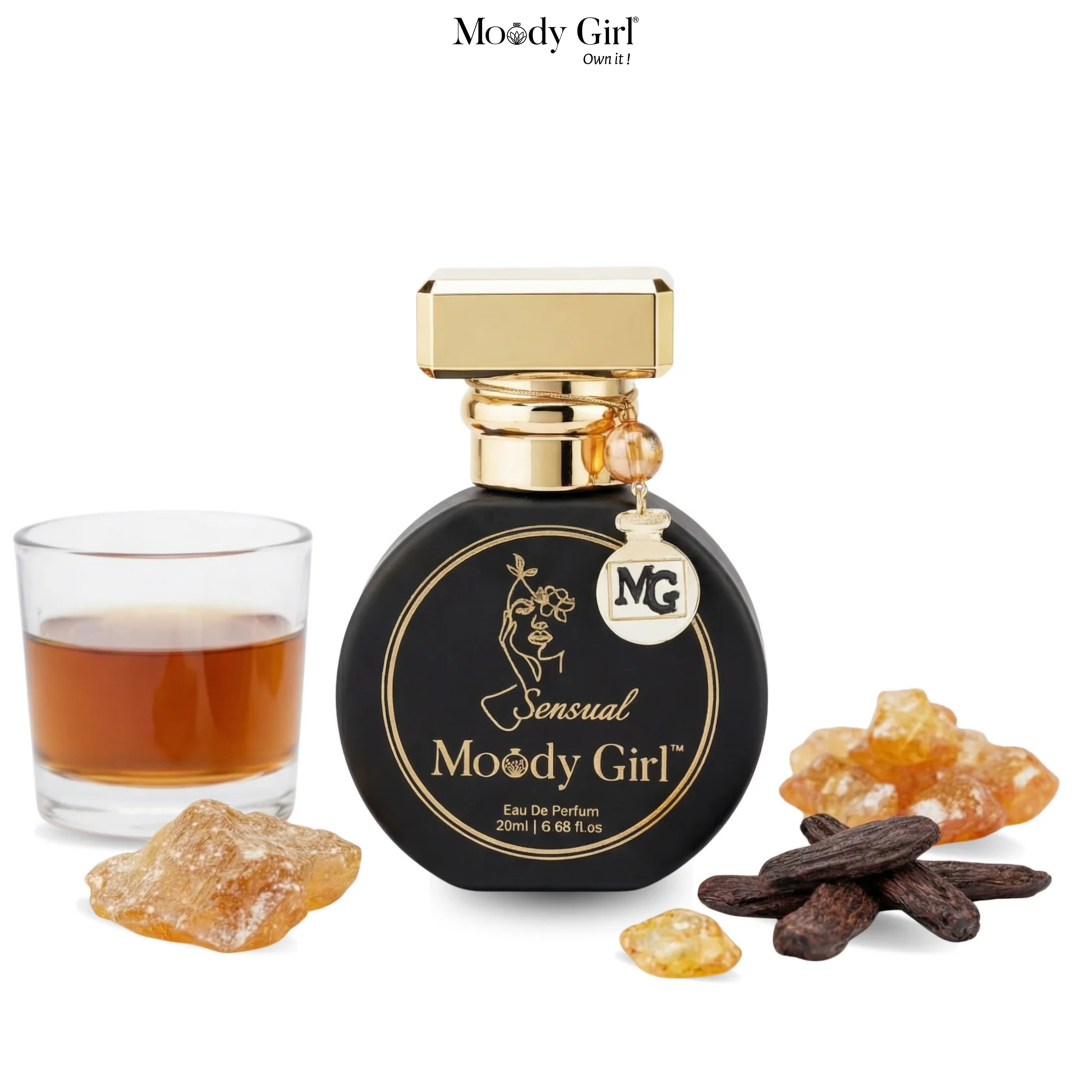 Moody Girl perfume bottle with a glass of amber liquid and natural elements on a white background