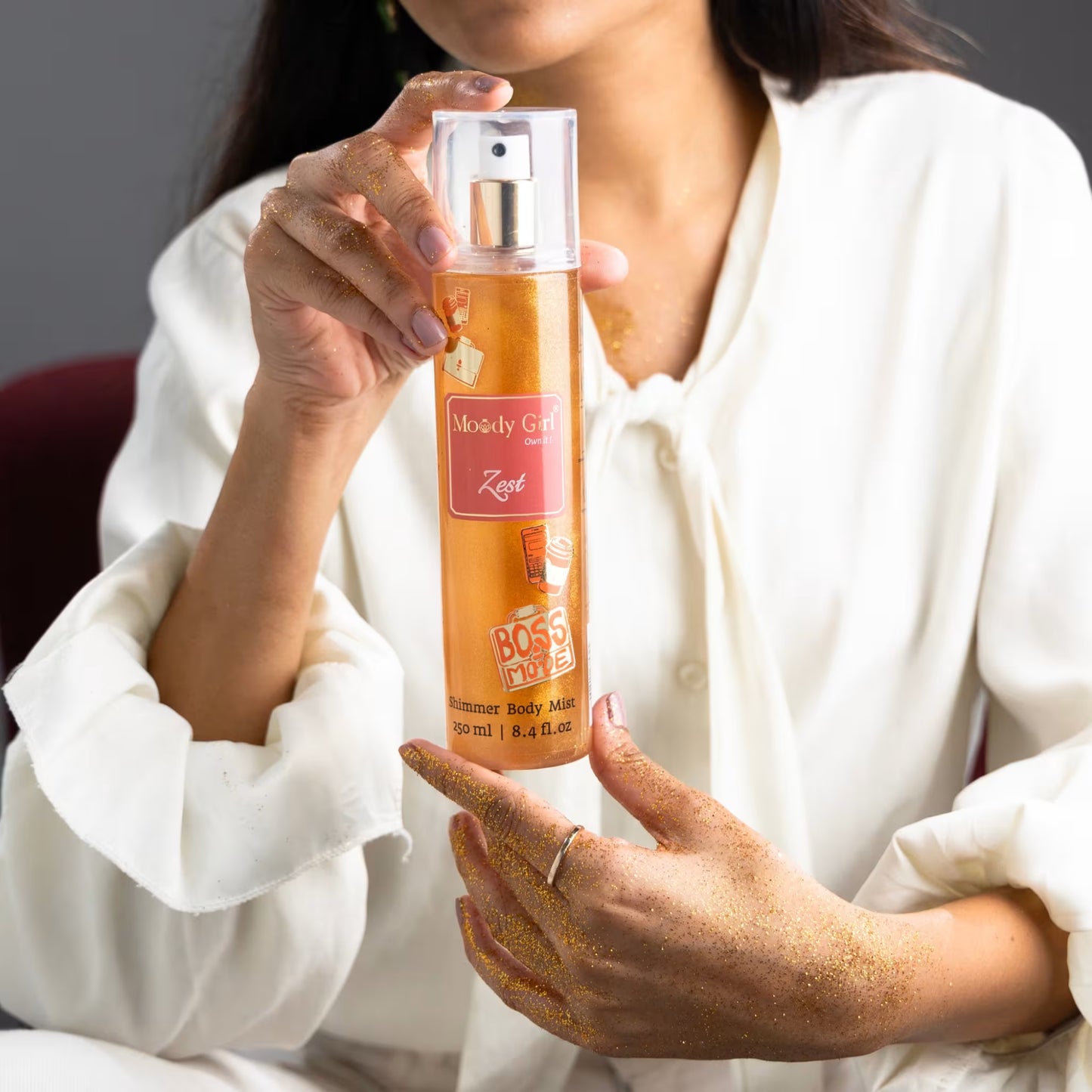 A person holding a bottle of Zest shimmer body mist with visible branding of Moody Girl