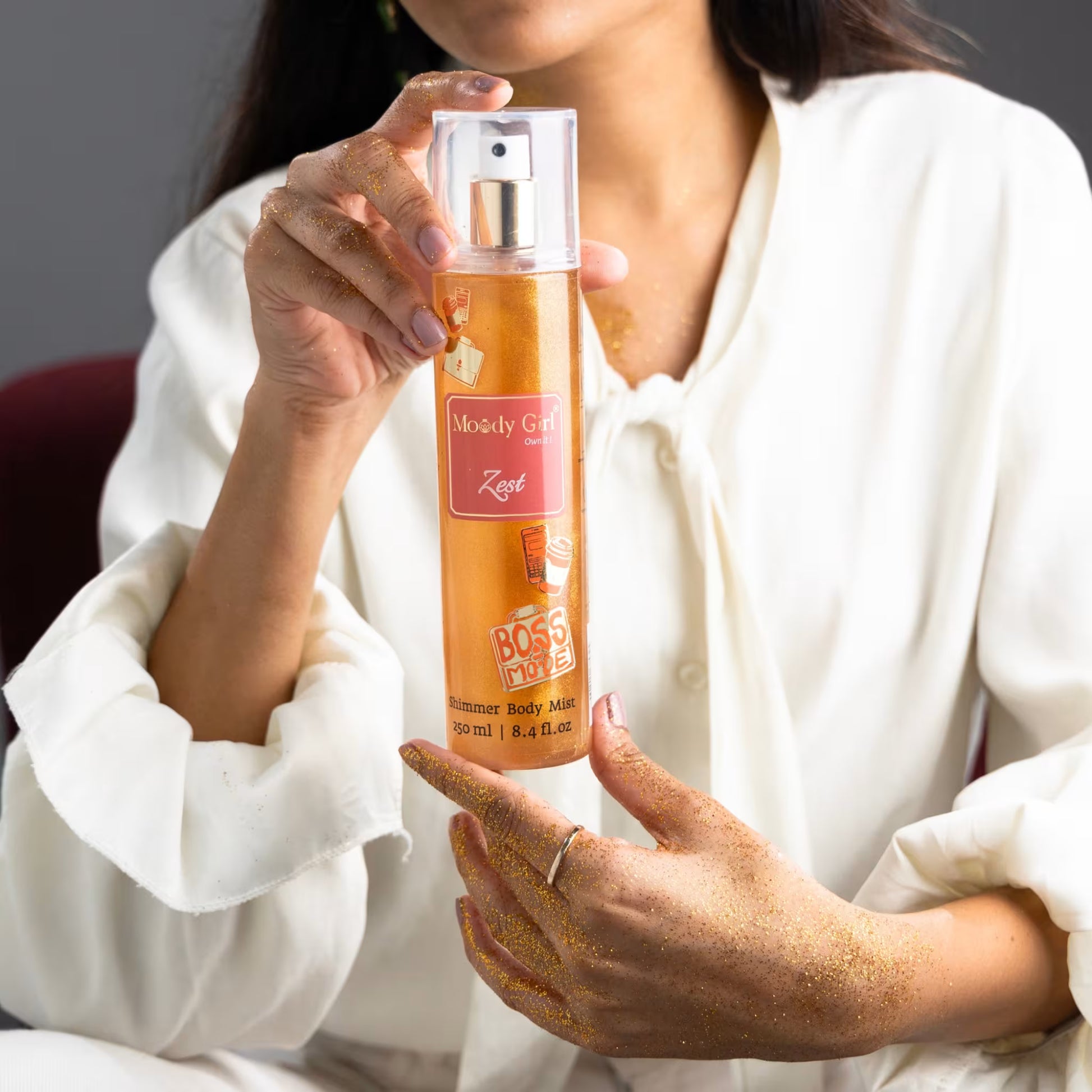 A person holding a bottle of Zest shimmer body mist with visible branding of Moody Girl