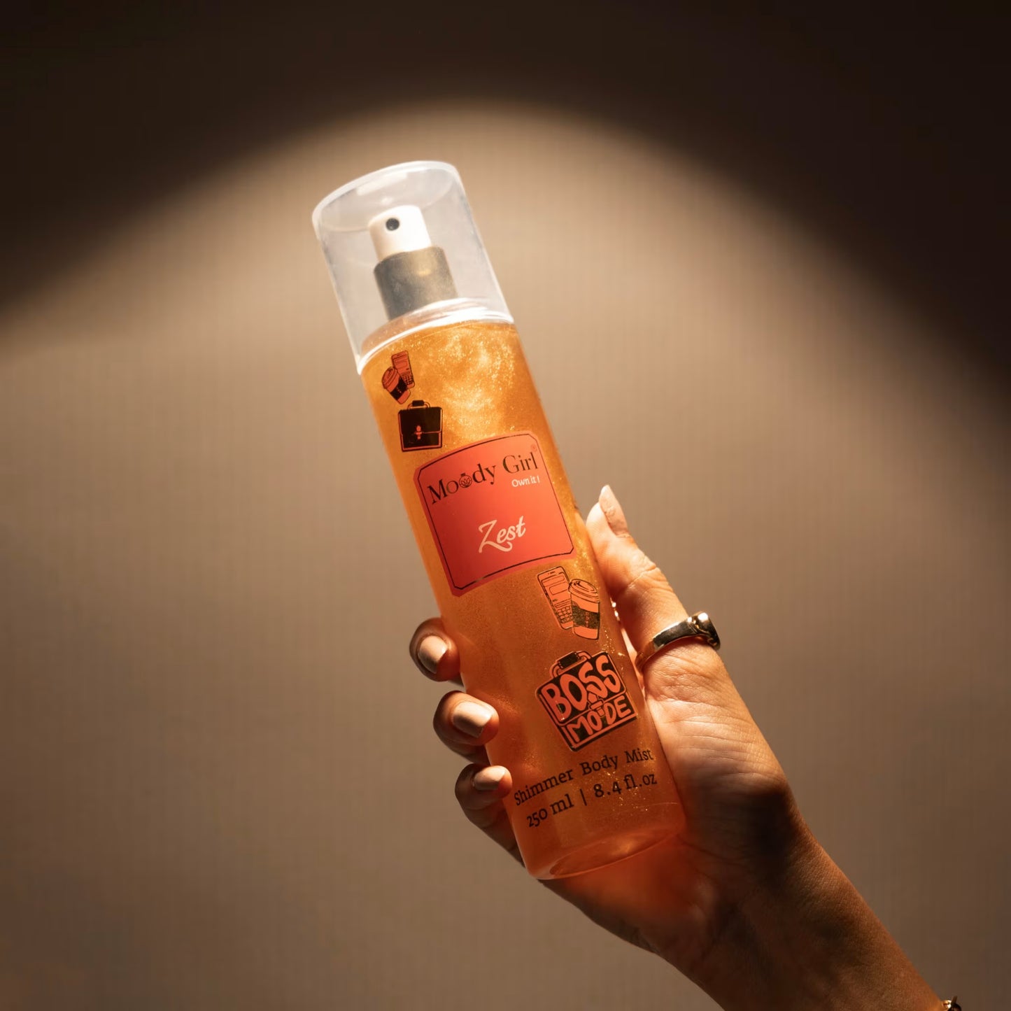 Hand holding a bottle of Zest shimmer body mist against a dark background