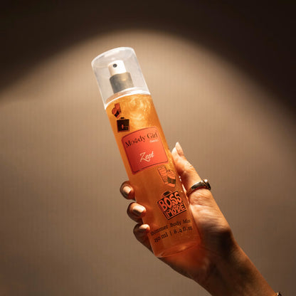 Hand holding a bottle of Zest shimmer body mist against a dark background