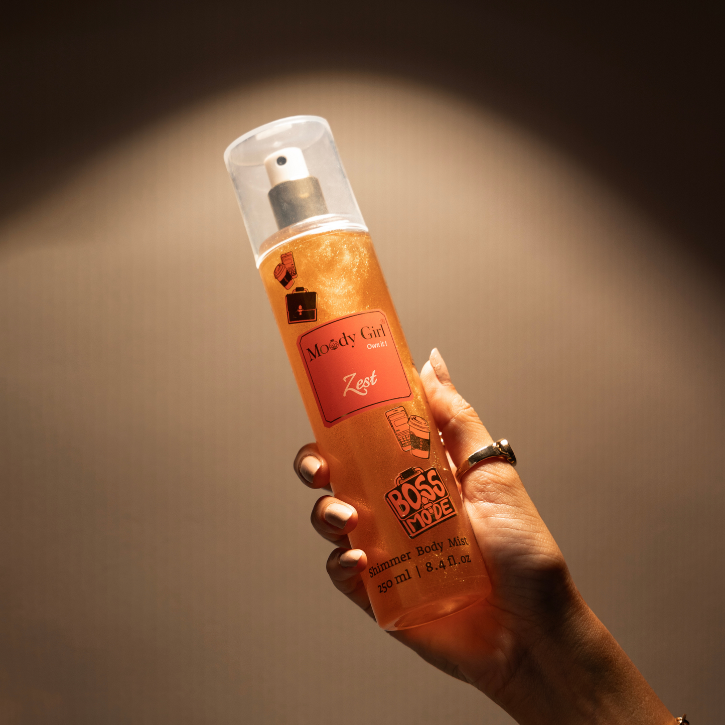 Hand holding a bottle of Boss Moze body mist with a warm glow on a brown background