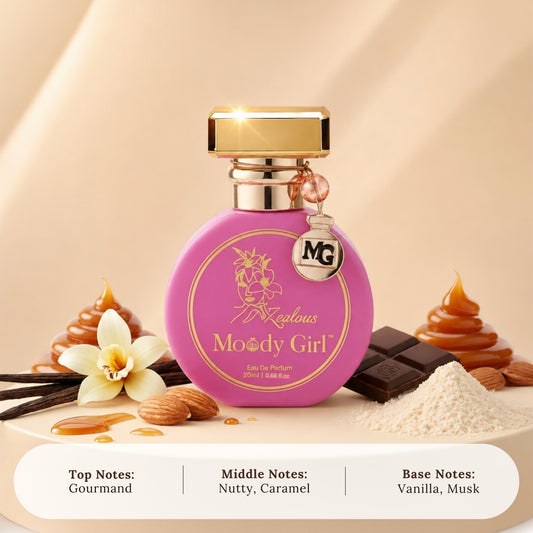 A pink oval perfume bottle with a gold cap and a hanging MG charm, labeled 'Magical Moody Girl' and 'Eau De Parfum 20ml'. The bottle is styled with chocolate, caramel, vanilla flower, almonds, and powder on a beige surface with a warm gradient background.